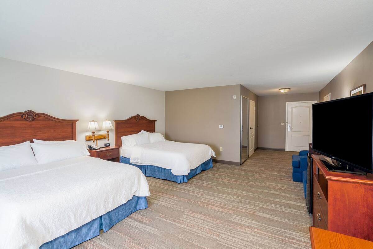 Habitación de hotel con dos camas, un televisor, un escritorio con lámpara y una puerta que da a otra habitación.