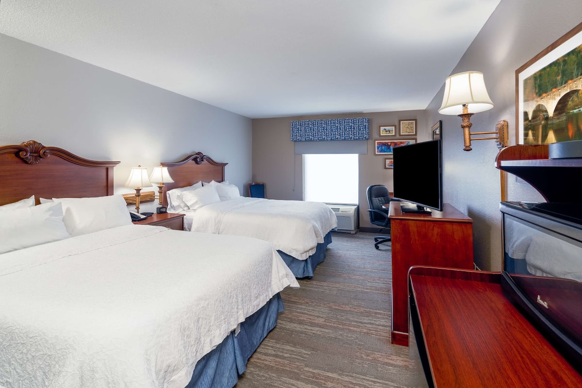 A hotel room with two beds, a desk, a TV, and a painting on the wall.