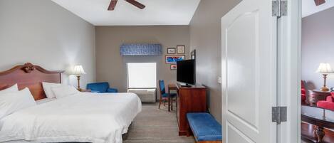 Ein Hotelzimmer mit Bett, Schreibtisch, Stuhl, Fernseher und Deckenventilator.