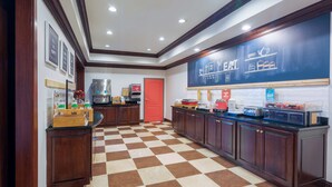 A hotel kitchen with checkered flooring, wooden cabinets, a chalkboard with writing, and various kitchen appliances.