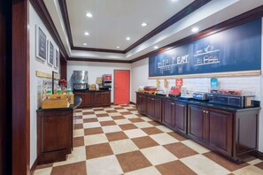 A hotel kitchen with checkered flooring, wooden cabinets, a chalkboard with writing, and various kitchen appliances.