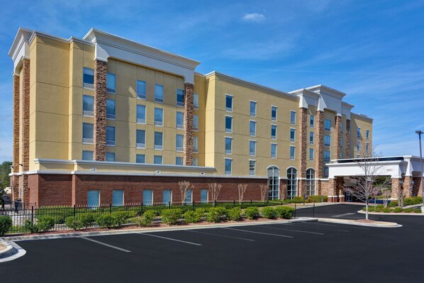 A multi-story hotel with a brick facade, large windows, and a parking lot in front.