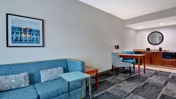 Una sala moderna con un sofá azul, una mesita pequeña y una cocina con armarios de madera y un espejo redondo.