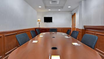 Una sala de conferencias con una gran mesa de madera, seis sillas, un televisor en la pared y una lámpara sobre la mesa.