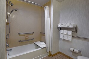 A bathroom with a bathtub, shower, towel rack, and toilet paper.
