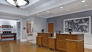 A hotel reception area with a wooden reception desk, a clock, and a 'happy' balloon wall decoration. - Hampton Suites Birmingham Hoover (Birmingham)