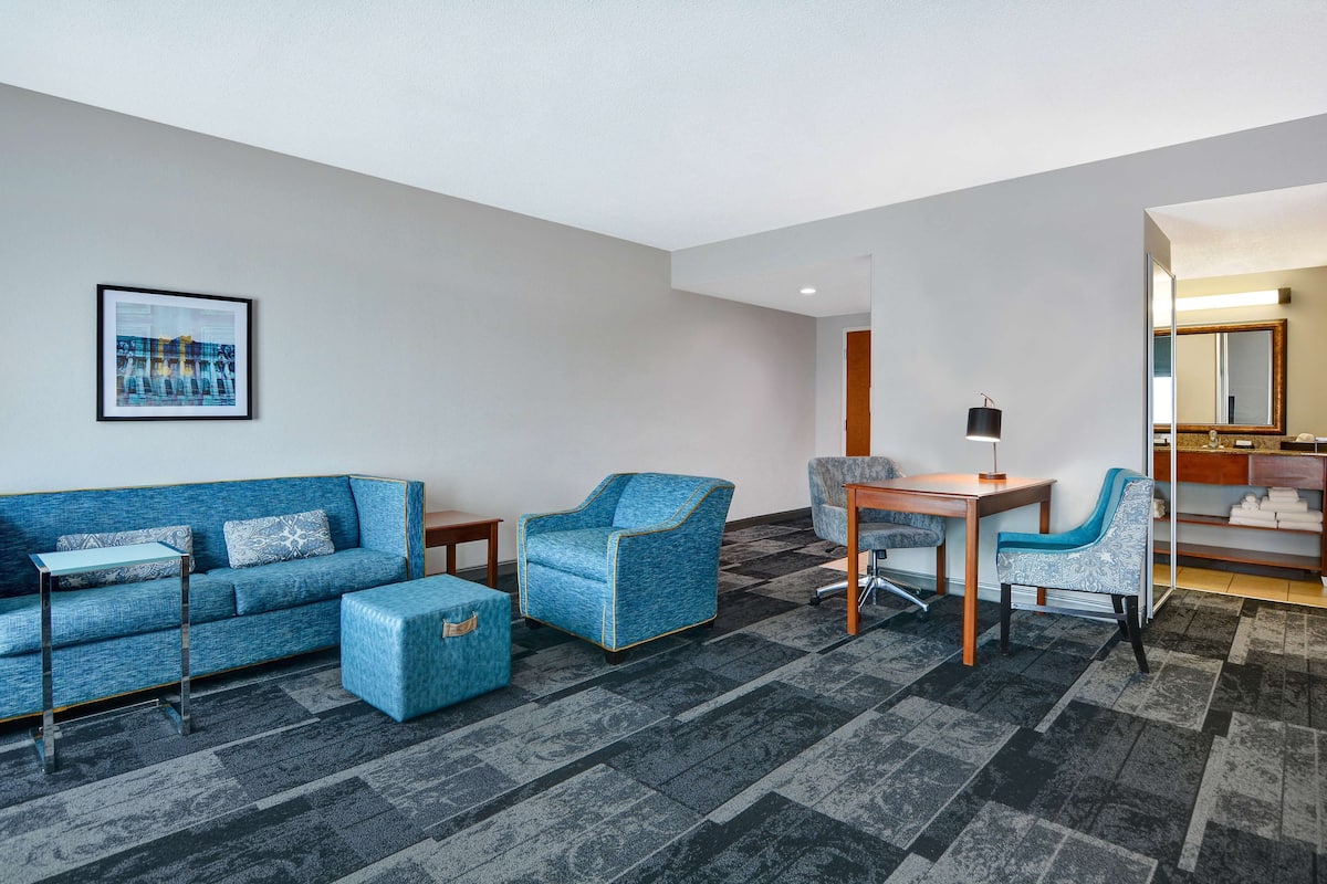 A modern living room with a blue sofa, matching armchair, and ottoman, a wooden dining table with two chairs, and a carpeted floor.