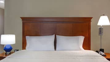 Une chambre d’hôtel avec une tête de lit en bois, un couvre-lit blanc, deux oreillers blancs, une lampe bleue et une lampe blanche sur une table de chevet.