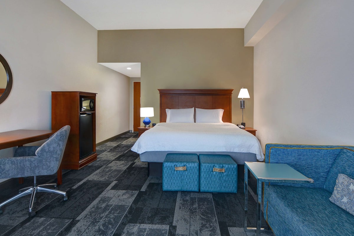 A hotel room with a bed, a desk, a chair, a sofa, and a small table.