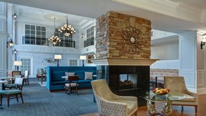 A spacious living area with a stone fireplace, blue sofa, and patterned armchairs. - Hampton Suites Birmingham Hoover (Birmingham)