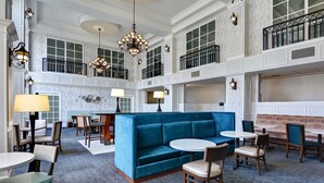A spacious lobby with a blue sofa, round tables, and chairs, a chandelier, and a balcony with a railing. - Hampton Suites Birmingham Hoover (Birmingham)
