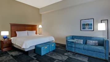 A hotel room with a bed, a blue sofa, a nightstand, and a lamp.