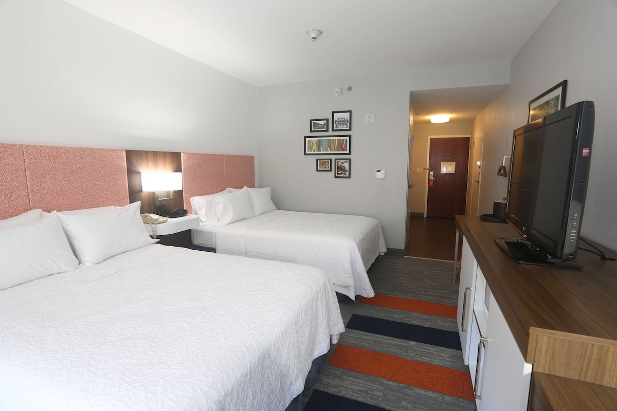 A hotel room with two beds, a desk with a television, and a hallway leading to another room.