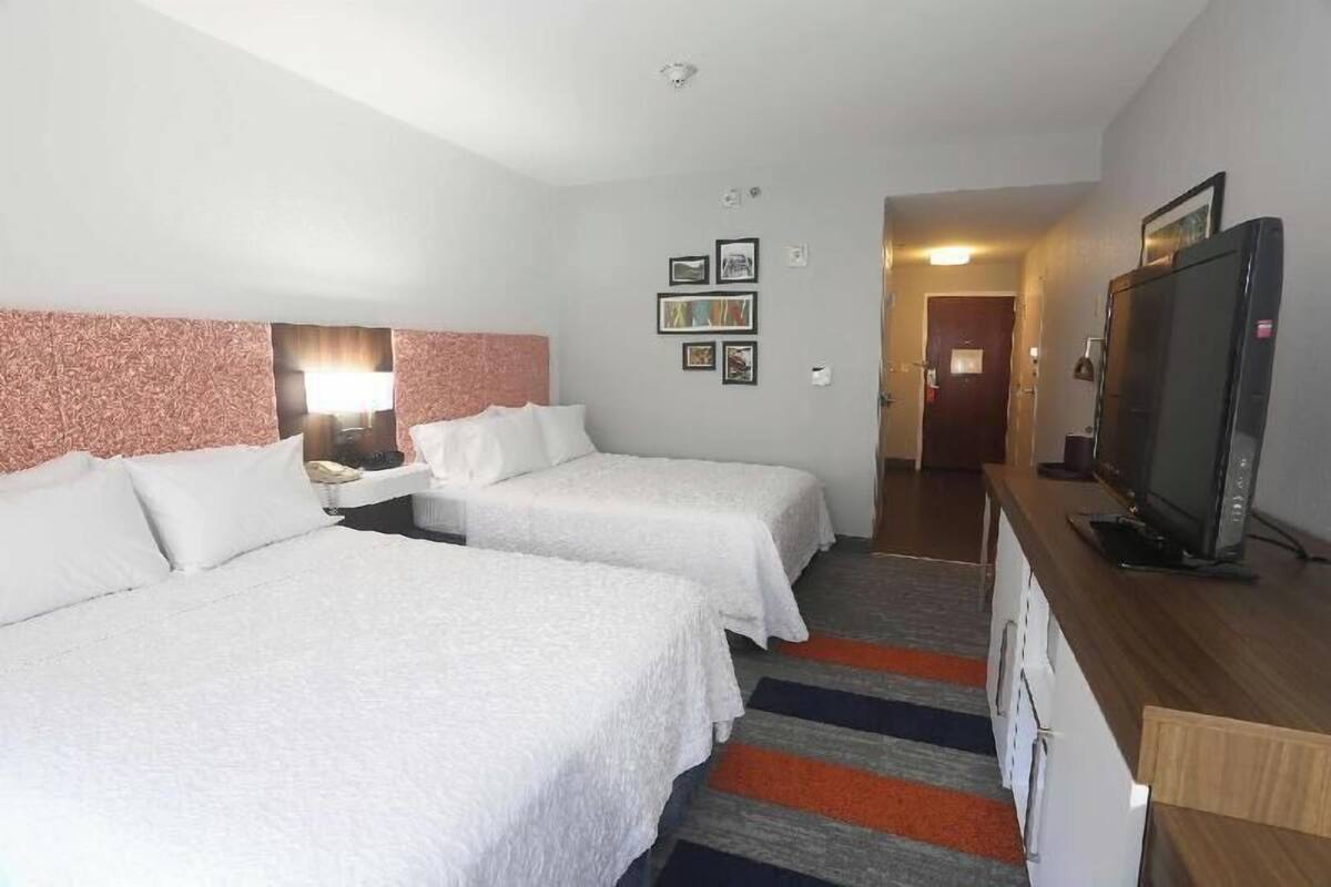 Habitación de hotel con dos camas, un televisor, un escritorio y un pasillo que conduce a otra habitación.