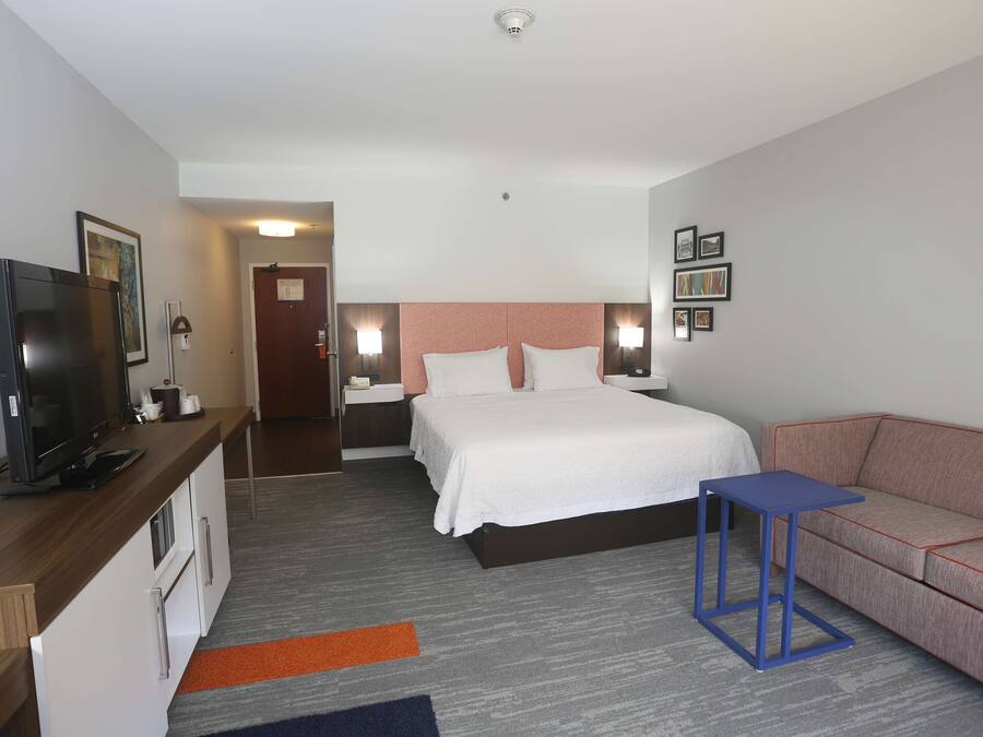Una habitación de hotel con cama, mesitas de noche, televisor, escritorio y sofá.