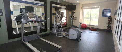 Un gimnasio con cintas de correr, elípticas y pelotas de ejercicio.
