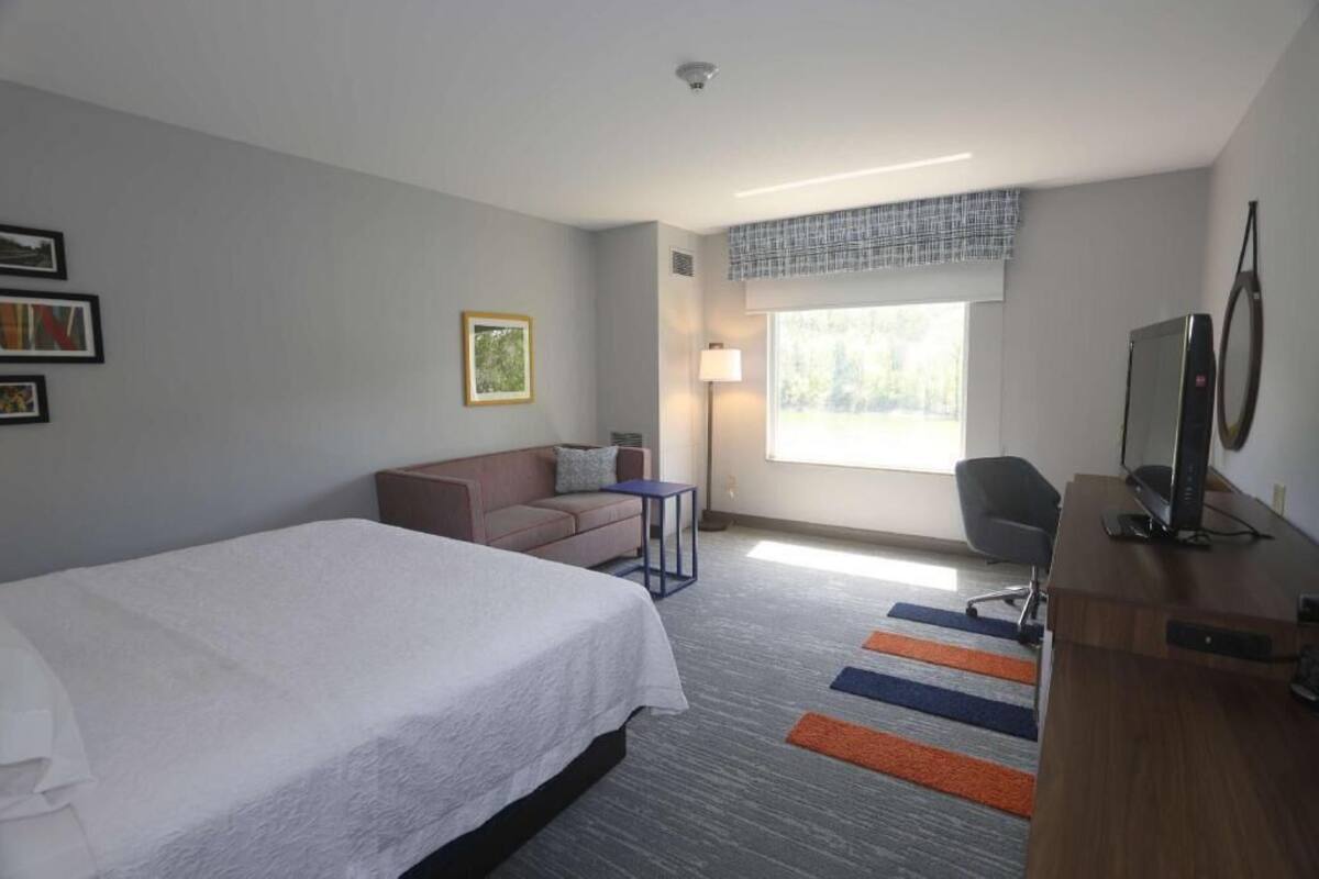 Habitación de hotel con cama, escritorio, silla, sofá, lámpara y ventana con vistas.