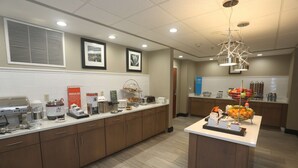 A modern kitchen with a long counter, coffee machines, and a fruit bowl.