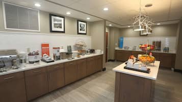 A modern kitchen with a long counter, coffee machines, and a fruit bowl.