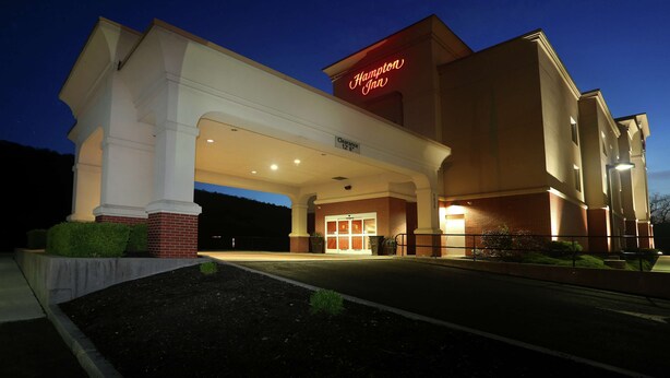 A Hampton Inn hotel entrance at dusk with a clear sign, a covered walkway, and a landscaped area.