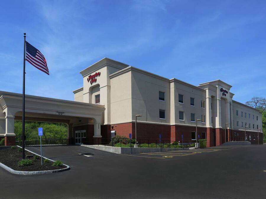A Hampton Inn hotel with a clear sky, parking lot, and American flag.