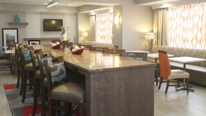 A modern hotel dining area with a central island, seating arrangements, and a television on the wall.
