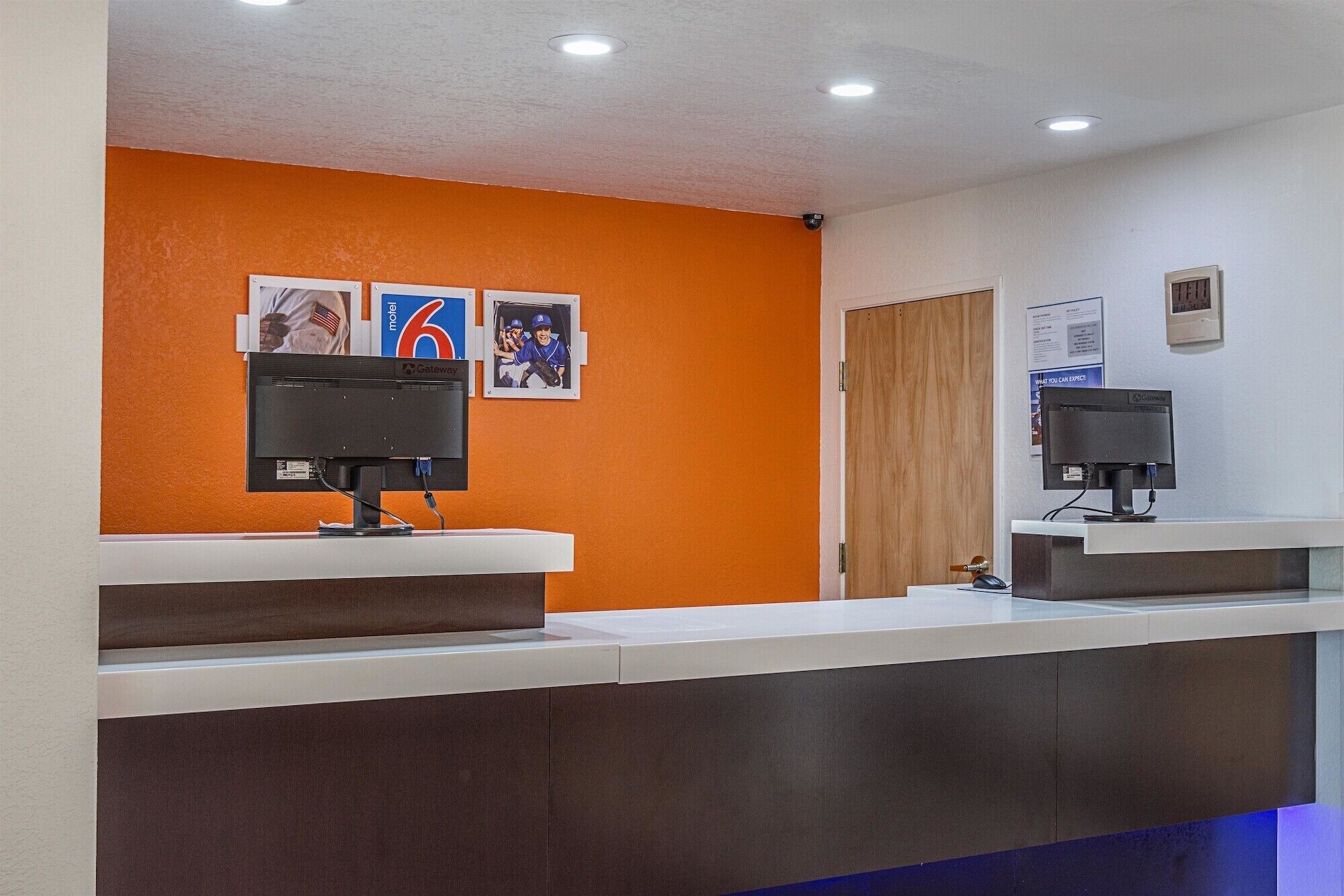 A reception desk with two computer monitors, a wooden door, and a wall with three framed pictures.
