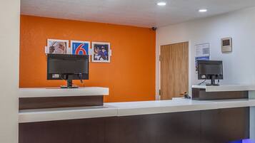 A reception desk with two computer monitors, a wooden door, and a wall with three framed pictures.