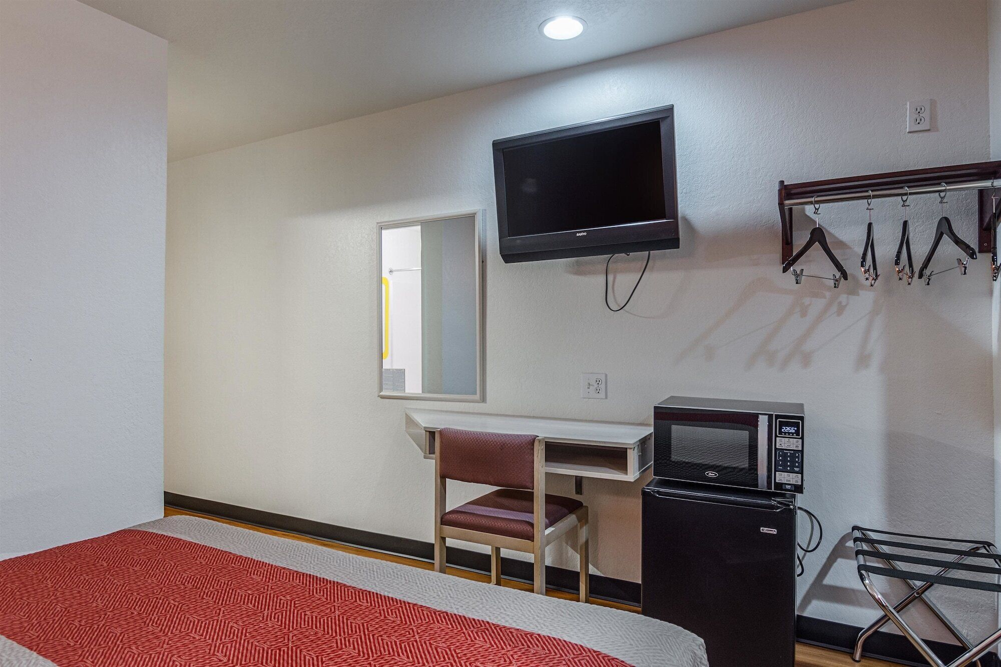 Habitación de hotel con cama, escritorio y silla, televisión, microondas y perchero con perchas.
