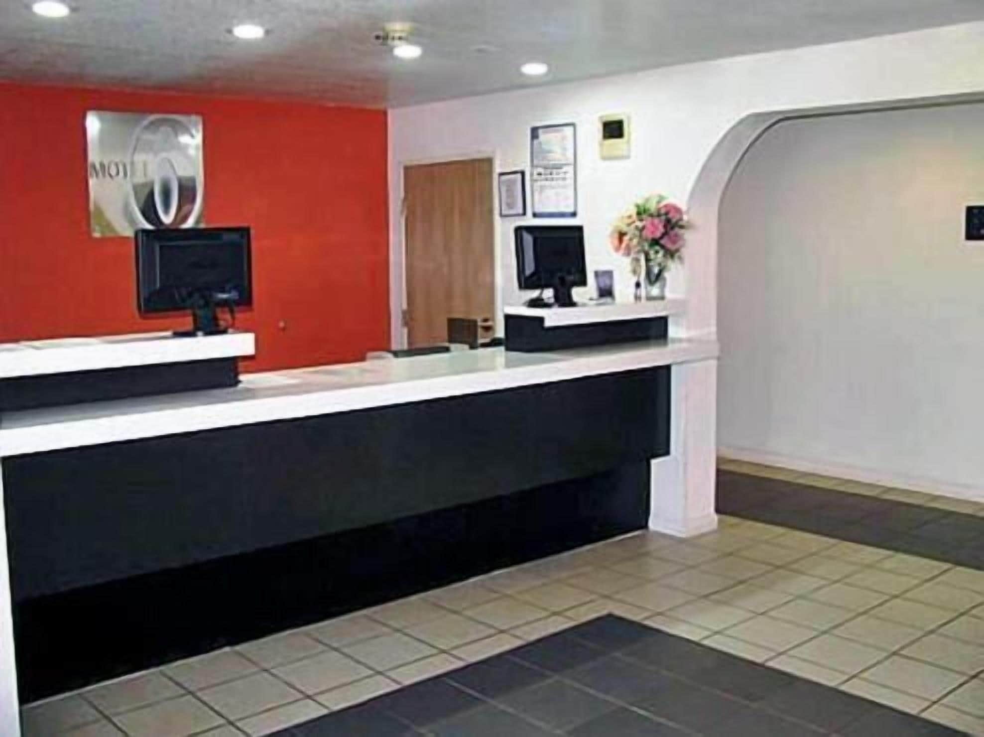 A reception desk with a red wall, a black counter, and a monitor.