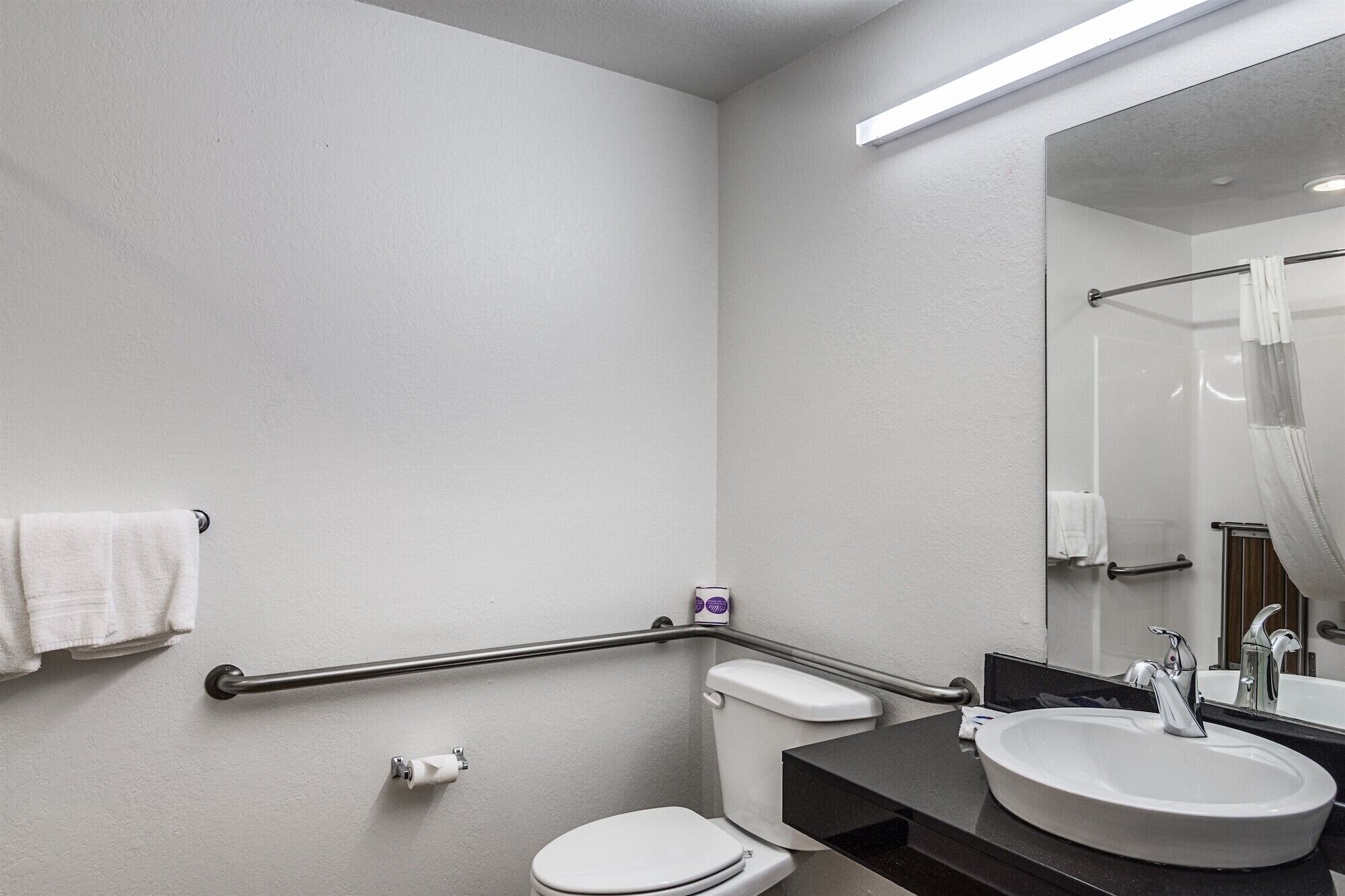 Un baño con inodoro, lavamanos, espejo y barandilla.