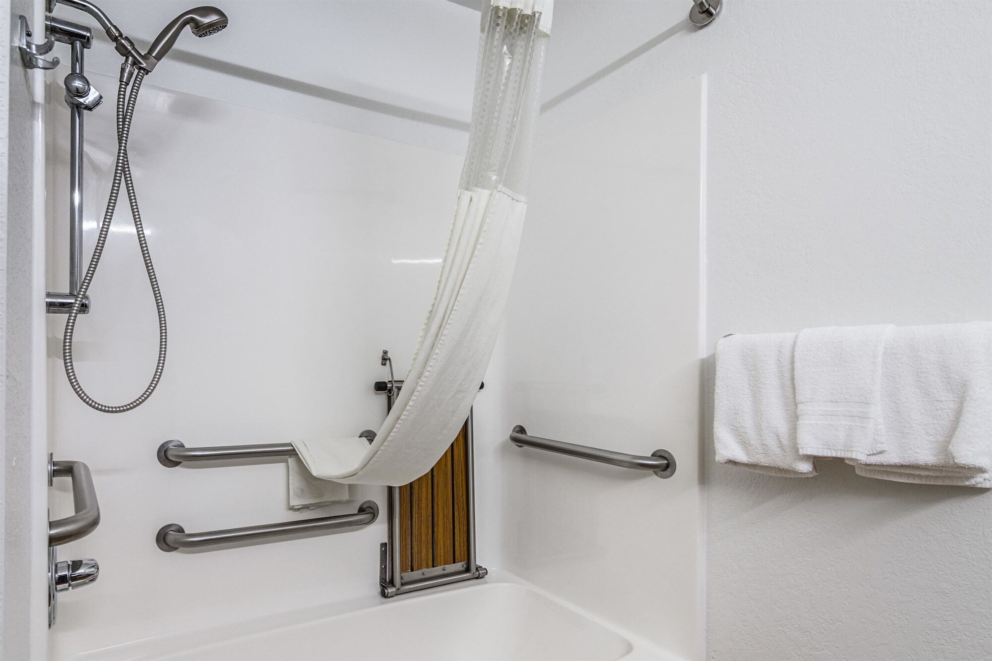 A bathroom with a white bathtub, a shower with a handheld showerhead, and grab bars.
