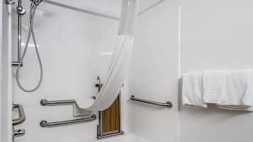 A bathroom with a white bathtub, a shower with a handheld showerhead, and grab bars.