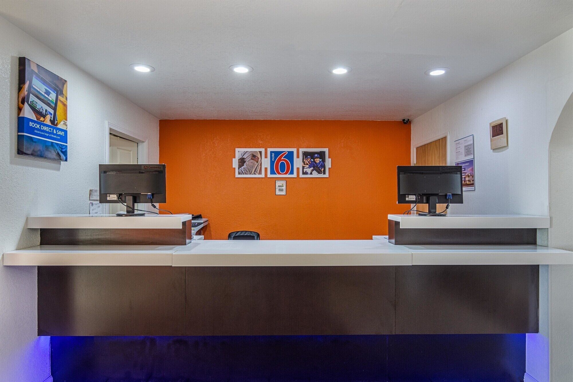 Un comptoir d’accueil doté de deux écrans d’ordinateur, d’un plan de travail blanc et d’un mur orange orné de tableaux.