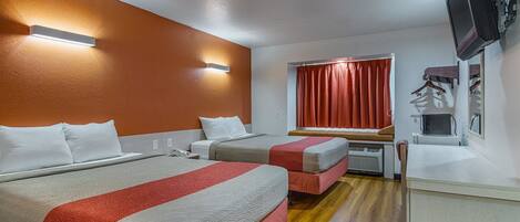 Habitación de hotel con dos camas, televisión, escritorio y ventana con cortinas.