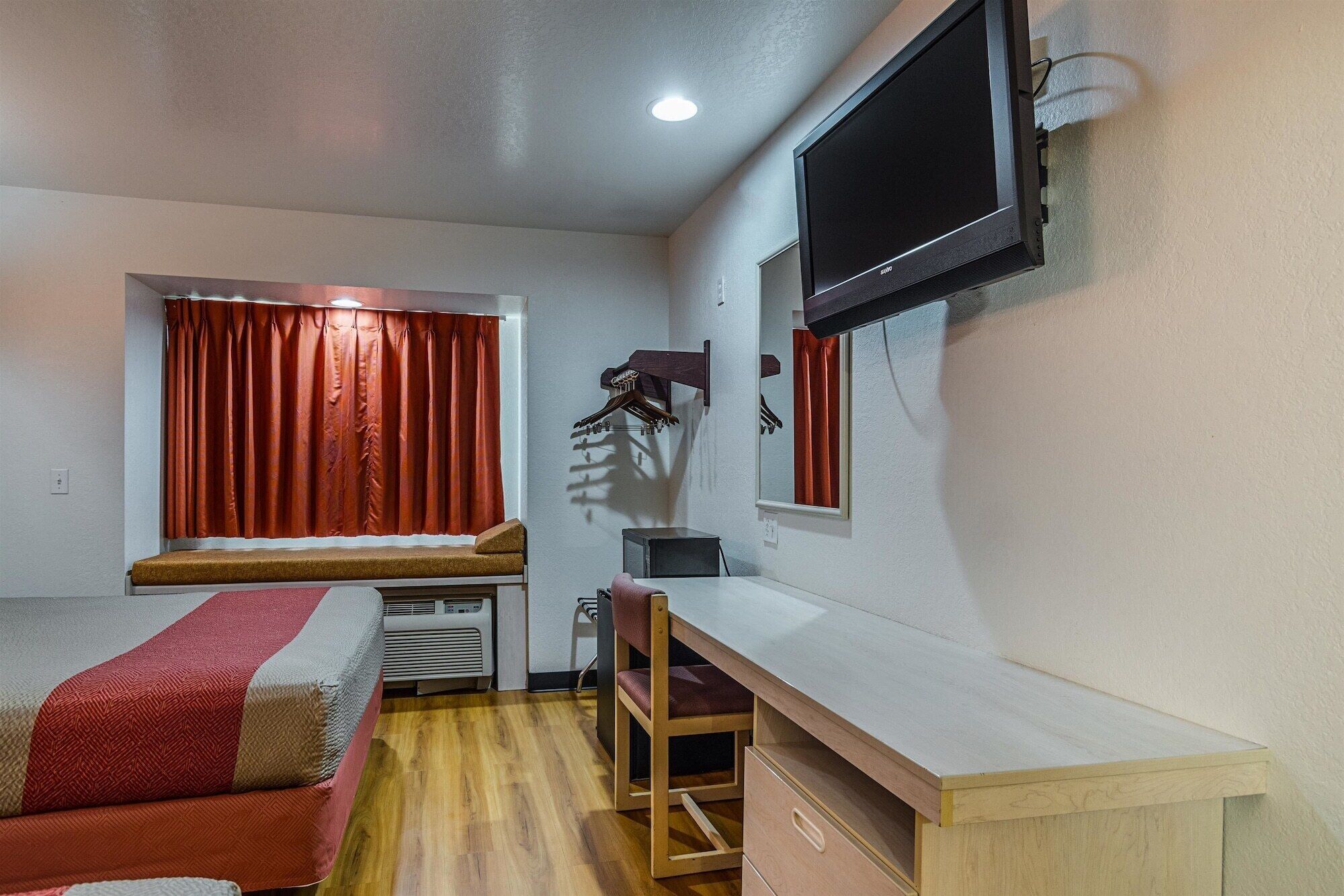A compact room with a bed, a desk, a chair, a TV, and a window with curtains.