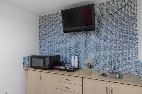A kitchenette with a microwave, a small sink, and a television mounted above the counter.