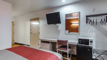 Quarto de hotel com uma cama, escrivaninha, cadeira, televisão, micro-ondas e um pequeno frigorífico.