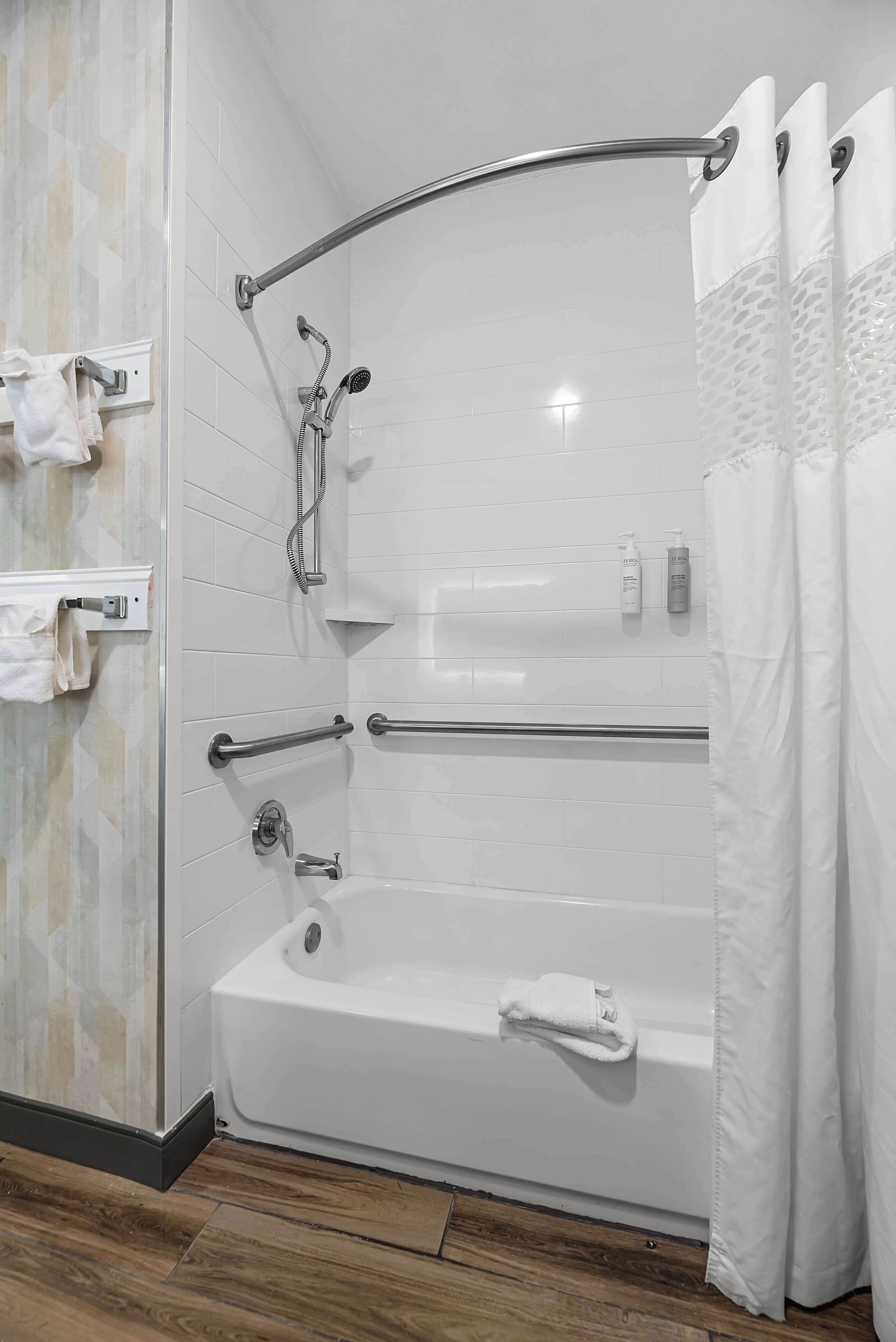 A modern bathroom with a walk-in shower, grab bars, a bathtub, and a glass-enclosed shower area.