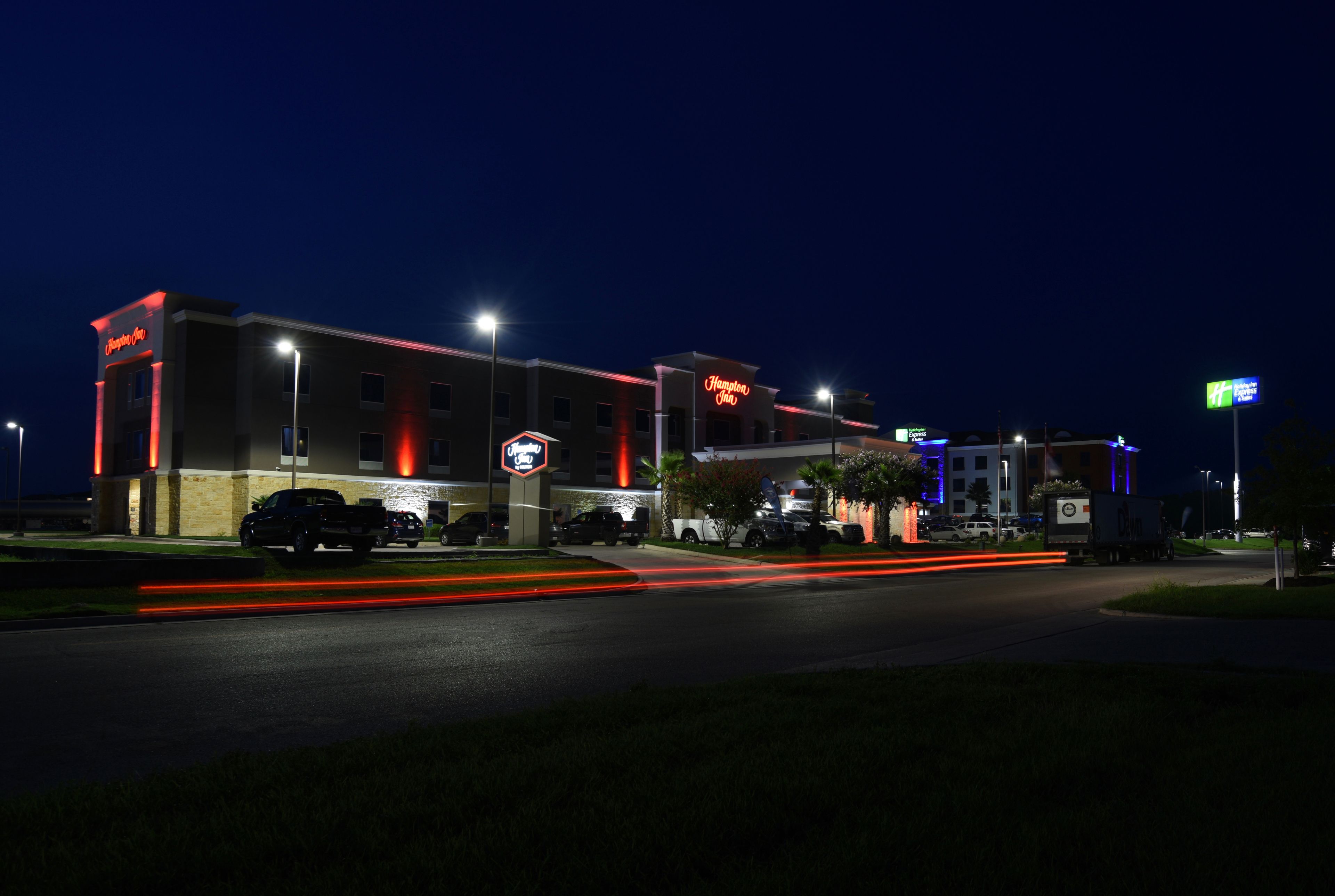 A hotel with a prominent sign, a parking lot, and a well-lit entrance.