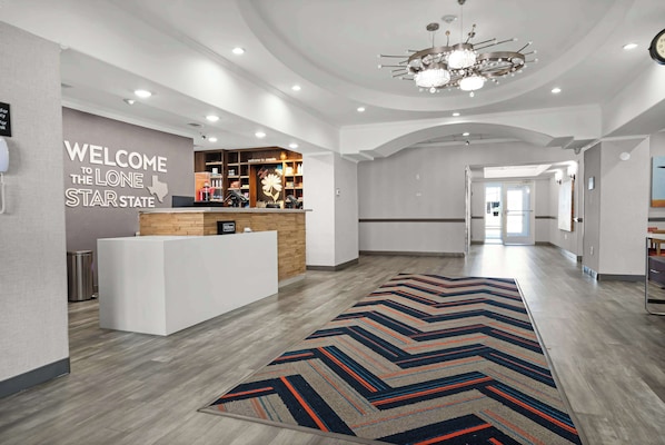 A hotel lobby with a reception desk, a welcome sign, and a modern chandelier.