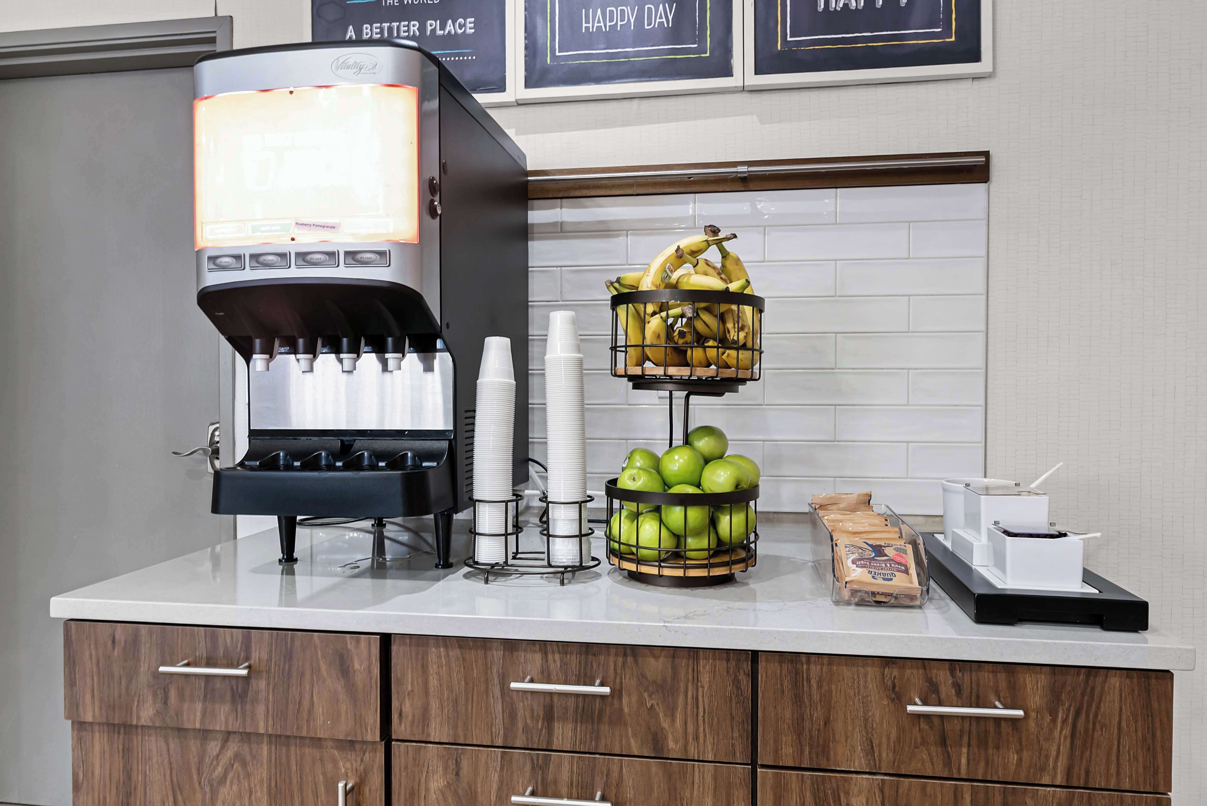 Una cafetera, una cesta de frutas con plátanos y manzanas, y un dispensador de café en una encimera.