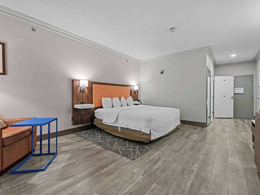 A modern hotel room with a bed, a small table, a sofa, and a bathroom visible through an open door.