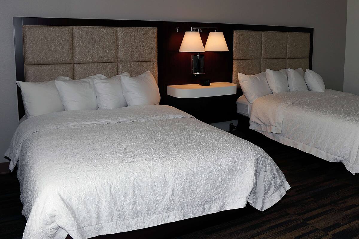 Habitación de hotel con dos camas, una mesita de noche con lámpara y cabecero con diseño texturizado.