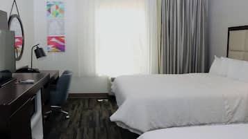 A hotel room with two beds, a desk with a chair, a desk lamp, and a window with curtains.