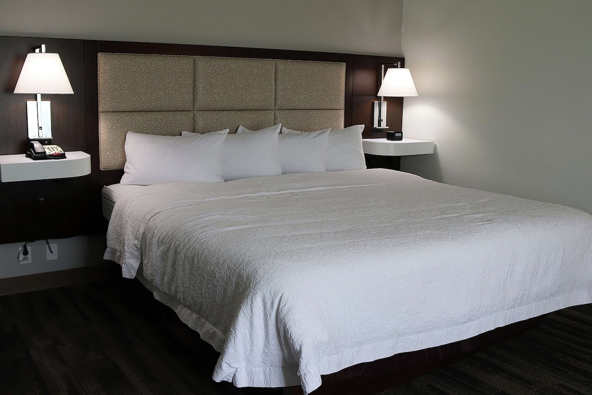 Habitación de hotel con una cama grande, dos mesitas de noche con lámparas, un teléfono y un panel en la pared.