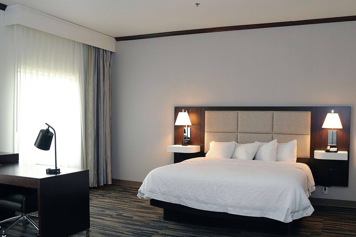 Habitación de hotel con una cama grande, dos lámparas de noche, un escritorio con silla y una ventana con cortinas.