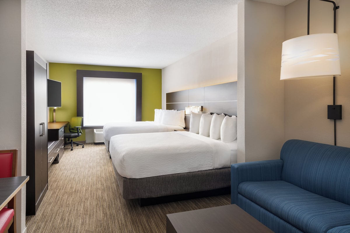 A hotel room with a large bed, a desk with a chair, a blue sofa, and a large window.