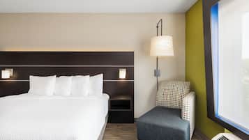 Ein Hotelzimmer mit einem großen Bett, einem Nachttisch mit Lampe, einer kleinen Sitzecke und einem Fenster mit Jalousien.