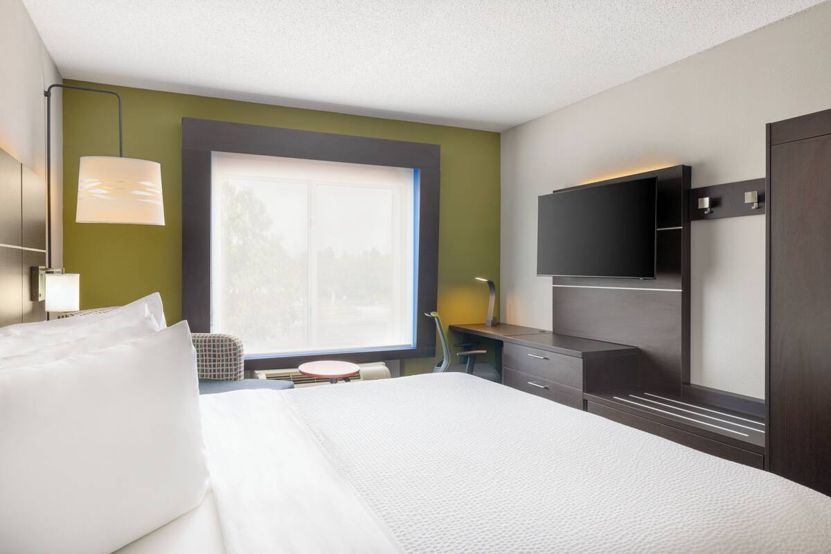 A hotel room with a bed, a desk, a chair, a TV, and a window with a view.